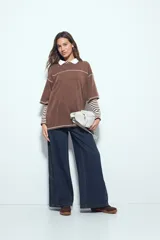 Remera de manga corta color marrón con efecto desgastado, corte oversize y costuras a la vista en color blanco. Presenta cuello redondo con cuello polo blanco superpuesto y mangas largas a rayas horizontales marrones y blancas por debajo.