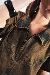 Vestido corto marrón con efecto desgastado, cuello camisero, cierre frontal con cremallera metálica, mangas cortas, dos bolsillos frontales y bordados de soles en el canesú delantero y trasero.