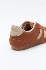 Zapatilla urbana de perfil bajo con diseño retro, confeccionada en poliuretano con detalles en textura tipo gamuza. Presenta puntera redondeada, cordones clásicos y suela de goma color caramelo.
