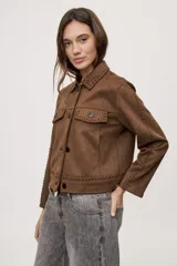 Campera negra de efecto gamuzado con cuello camisero, cierre frontal de botones, bolsillos plaqué en el pecho y detalles de costuras decorativas y calados.