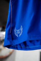 Short deportivo azul con cintura elástica, bolsillos laterales y logo estampado en la pierna izquierda.