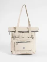 Mochila shopper color beige, confeccionada en poliéster. Presenta un diseño versátil con múltiples cierres, compartimento inferior expandible y un bolsillo frontal removible que funciona como estuche. Incluye correas ajustables y removibles para usar como mochila o bandolera, además de asas fijas para llevar al hombro.