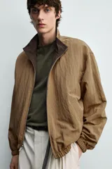 Cazadora bomber reversible de corte relaxed fit, color marrón oscuro, con cuello alto, cierre frontal de cremallera, bolsillos laterales de vivo y acabados elásticos en puños y dobladillo.