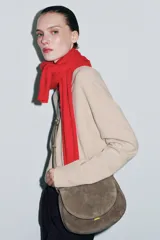 Bolso bandolera de piel gamuzada color gris topo, con solapa curva, asa de mano corta y herrajes metálicos dorados.