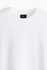 Remera blanca de manga larga en punto de algodón de peso medio, con cuello redondo acanalado, hombros caídos, puños acanalados y bajo recto. Presenta un corte holgado.