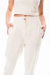 Pantalón de vestir color crudo, de corte recto, con bolsillos laterales y traseros. Se ajusta a la cintura con cinturón de cuero marrón.