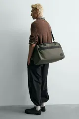 Bolso de viaje tipo duffel bag, color negro, con acabado engomado y costuras visibles. Cuenta con dos asas de mano y una correa de hombro ajustable y extraíble. Posee múltiples compartimentos con cierre de cremallera.