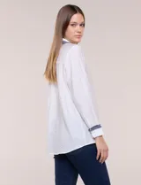 Camisa de crepe liviana y texturada color blanco, de silueta relajada y holgada, con cuello camisero clásico y puños con detalles de bordado de pasamanería con terminación deshilachada y aplique de perlas. Cuenta con cartera de botones oculta al frente y mangas largas.