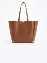 Cartera tipo shopper de cuero vacuno con textura graneada. Presenta un diseño amplio y flexible con manijas largas para llevar al hombro y cierres laterales decorativos con tiradores personalizados.