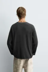 Jersey de manga larga, cuello redondo y calce relajado, color negro con efecto lavado y textura tejida.