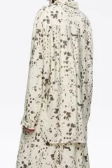 Camisa de corte recto con cuello camisero, mangas largas y puños abotonados. Presenta un estampado abstracto en tonos marrón oscuro sobre fondo crema.