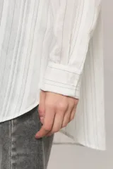 Camisa oversize de manga larga en color blanco con diseño de sutiles rayas verticales a tono y contratono, cuello camisero, bolsillo frontal en el pecho y cierre delantero con botones.