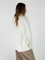 Sweater de cuello alto en color beige, con diseño de punto liso y terminaciones acanaladas en puños y ruedo. Presenta aberturas laterales en el bajo y un detalle de borde desflecado en el ruedo y los puños.