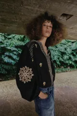 Camisa negra de manga larga con cuello redondo y escote en V, adornada con bordados florales en contraste en tonos beige y marrón a lo largo de la abertura frontal, hombros y mangas.