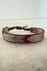 Pulsera tejida artesanalmente con cuentas Miyuki en una paleta de colores que combina tonos beige, marrones, bordó y oro rosa. Presenta un diseño ajustable mediante un cordón marrón.
