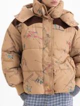 Campera puffer color tostado con estampado de figuras esquiando, capucha desmontable, recortes en corderoy marrón en los hombros, puños tejidos y cierre frontal con botones a presión.