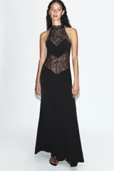 Vestido largo negro de cuello halter con detalles de encaje en la parte superior y espalda. Cuenta con corte en línea evasé y cierre posterior con abertura y botón.