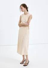 Vestido midi color beige, de cuello redondo y sin mangas, con diseño cruzado en la falda y lazo ajustable en la cintura.