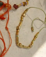 Collar artesanal compuesto por piezas metálicas irregulares con acabado dorado, ensartadas en un cordón de hilo de algodón natural. Presenta un sistema de nudo corredizo para ajustar el largo.