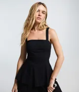 Blusa peplum de bengalina color negro, con escote recto y breteles anchos. Presenta un corte ajustado en el torso con un dobladillo con volados que aporta volumen y estructura a la silueta.
