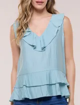 Blusa blanca sin mangas confeccionada en tejido de satén con suave textura arrugada y caída fluida. Cuenta con escote en V con volante en el cuello y ruedo estilo peplum con doble capa de volados superpuestos.