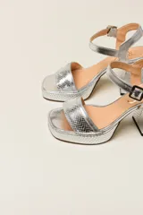 Sandalia de tacón grueso y plataforma, color dorado con textura de piel de serpiente. Cuenta con una tira ancha en la parte delantera y una correa ajustable al tobillo con hebilla.