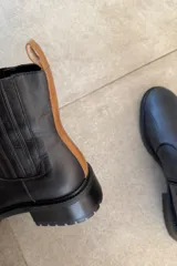Botin de cuero vacuno color marrón, con taco bajo y suela track. Presenta una franja vertical negra en la parte trasera y cierre lateral.