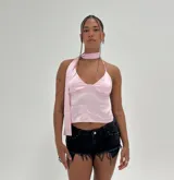 Top corto color rosa pálido con escote pronunciado en V y tirantes anchos que se anudan alrededor del cuello como una bufanda o corbata. El diseño es ajustado y deja los costados expuestos.