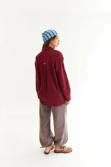 Camisa de corte oversize color bordó, con cuello camisero, mangas largas y bordado en hilo rojo en la espalda con la frase The Winter League. Presenta recortes con costuras a contratono y detalle de placa metálica pequeña en la parte superior trasera.