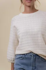Buzo de tejido liviano en color beige, con diseño calado de líneas horizontales, cuello redondo y mangas largas levemente abullonadas con terminaciones en rib.