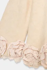 Jersey de punto color crema con cuello redondo y mangas tres cuartos. Presenta un diseño holgado con el ruedo decorado con aplicaciones de flores de tela en relieve.