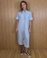 Vestido midi estilo túnica color celeste con rayas verticales blancas, cuello camisero, mangas cortas y cierre frontal con botones ocultos.