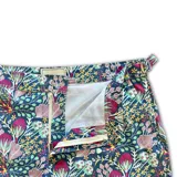 Short de baño con estampado floral y botánico en tonos violeta, rosa y verde sobre fondo oscuro. Presenta pretina fija con hebillas metálicas laterales para ajuste, cierre frontal con botón a presión, bolsillos laterales y bolsillo trasero.