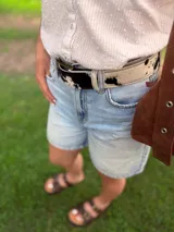 Cinto de cuero con forro de cuero, estampado animal print de vaca en blanco y negro, con hebilla metálica rectangular color bronce y broche suizo.