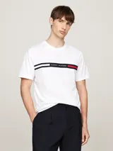 Remera blanca de algodón con cuello redondo y manga corta. Presenta una banda horizontal con los colores distintivos de Tommy Hilfiger y el logo bordado en el pecho.