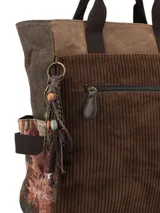 Mochila de diseño patchwork en tonos marrones, confeccionada en una combinación de pana, tela encerada y tejido estampado. Cuenta con un bolsillo frontal con cierre, manijas superiores fijas, correas ajustables y un llavero decorativo con borlas y cuentas colgando de un lateral.