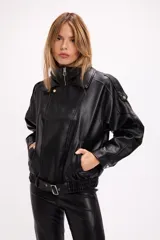 Campera estilo bomber oversize confeccionada en símil cuero negro con textura granulada. Presenta cuello alto con cierre frontal, hombreras marcadas, bolsillos laterales y cintura con elástico y cinto ajustable con hebilla metálica.