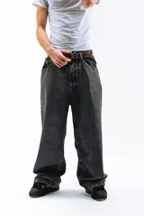 Pantalón de denim azul desgastado, corte mega baggy con piernas anchas y bolsillos traseros grandes. Presenta un bordado dorado en estilo gótico en el bolsillo trasero izquierdo.