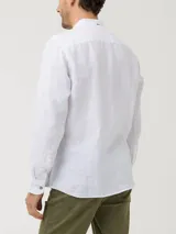 Camisa de manga larga confeccionada en lino orgánico, con cuello mao y cierre frontal de botones en tono madera. Presenta un diseño minimalista con bordado sutil al tono en el pecho.