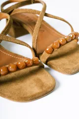 Sandalias de taco cuadrado medio, confeccionadas en gamuza color azul. Presentan tiras finas que cruzan el empeine, una pulsera ajustable al tobillo y detalle de cuentas decorativas en la tira frontal.