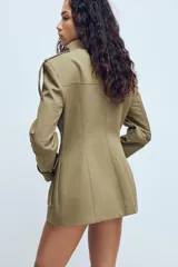 Chaqueta de estilo militar en color beige, con cuello subido, cierre frontal de botones, bolsillos de plastrón con solapa en el frente y detalle de hombreras con trabillas.
