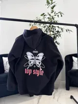 Canguro oversize negro con capucha y bolsillo tipo canguro. En la espalda presenta una estampa grande con diseño de mariposa, texto y la inscripción "top style" en color coral.