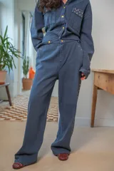 Pantalón de denim azul de corte amplio, con cierre de botón y cremallera, y detalles de tachas en los laterales y bolsillos.