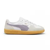 Championes Puma modelo Palermo LTH, con diseño de perfil bajo, cuerpo de cuero blanco, detalles en gamuza gris y franja lateral en color lila. Cuenta con suela de goma color caramelo y logo dorado en el lateral.