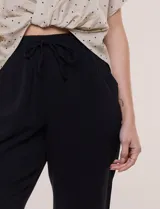 Pantalón capri negro de calce relajado y pierna recta, confeccionado en algodón. Posee cintura elastizada con cordón ajustable, bolsillos delanteros y detalle de presilla con botón en los ruedos.