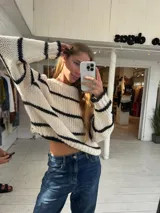 Buzo de tejido de punto grueso con diseño a rayas horizontales en color crudo y negro, cuello redondo y mangas largas.