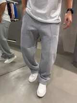 Pantalón de jogging baggy color gris melange, con cintura elástica, bolsillos laterales, costuras frontales en relieve y pequeño estampado con texto en la pierna izquierda.