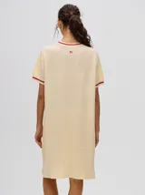 Vestido corto color amarillo claro, tipo remerón, de corte suelto con cuello redondo y mangas cortas. Presenta detalles de líneas en tono bordó en el cuello y en los puños.