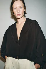 Blazer corto de color marrón oscuro, con cuello solapa, cierre frontal de botones y mangas largas con puños vueltos. Presenta un diseño con bajo elástico que le otorga una silueta ajustada en la cintura.