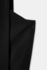 Vestido corto negro de escote asimétrico con detalle de bufanda integrada en el cuello y frunces laterales en el delantero. Presenta diseño sin mangas y cierre lateral con cremallera oculta.
